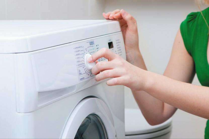 un enfant occupé fait la lessive, vide la machine à laver, nettoie